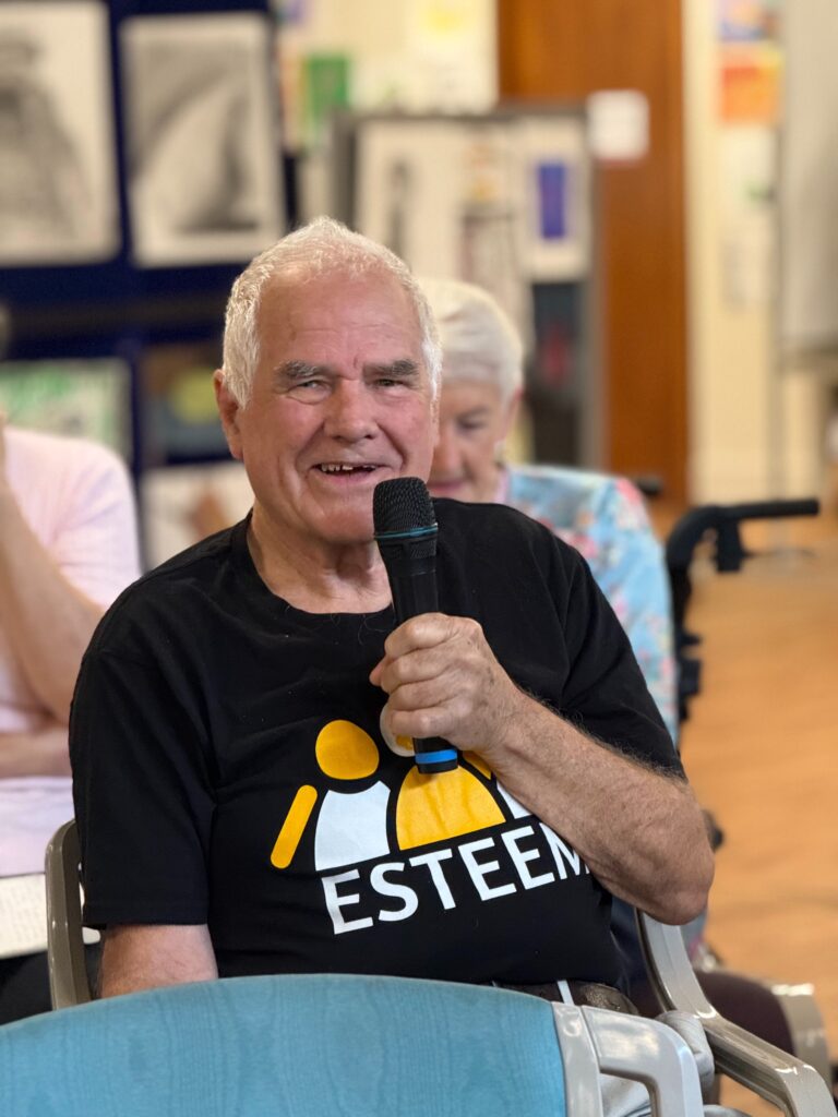A male ESTEEM stroke recovery participant sitting in a chair talking with a microphone in his hand.